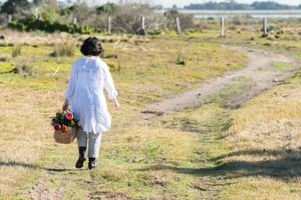 A woman walking down a country driveway with a basket of flowers